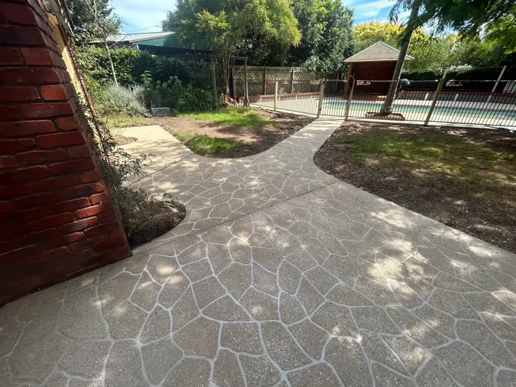 Decorative bush-rock pattern concrete path leading to a pool fence and pergola, Gippsland